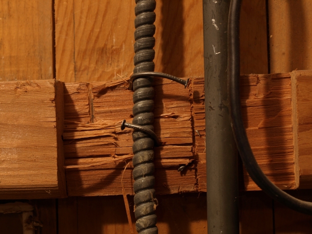 Image:  close up of electrical casing attached by bent nails to hacked up 2x4